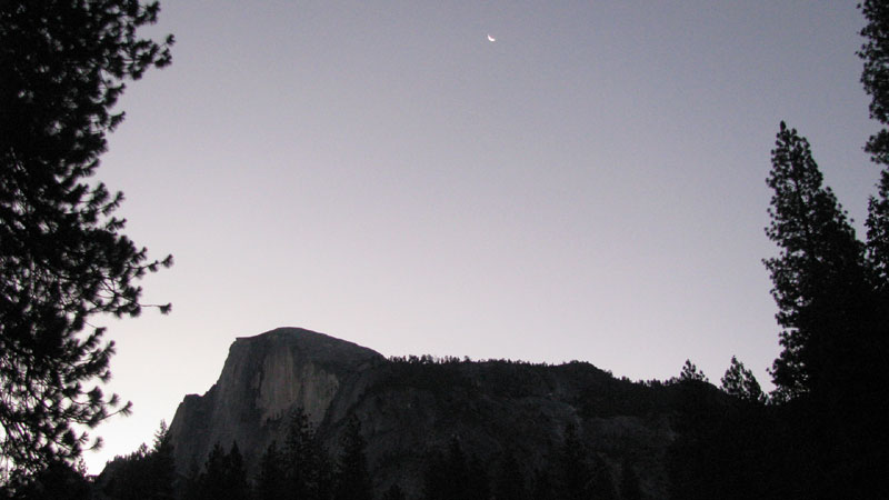 A crescent moon hangs over Half Dome